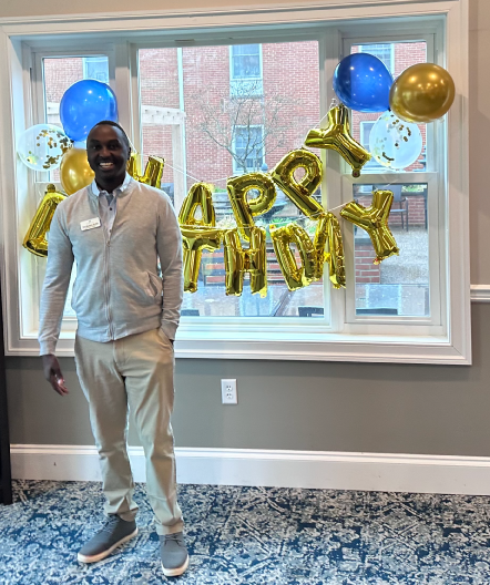 Foulk Living employee Tirus standing in front of his Happy Birthday balloon banner