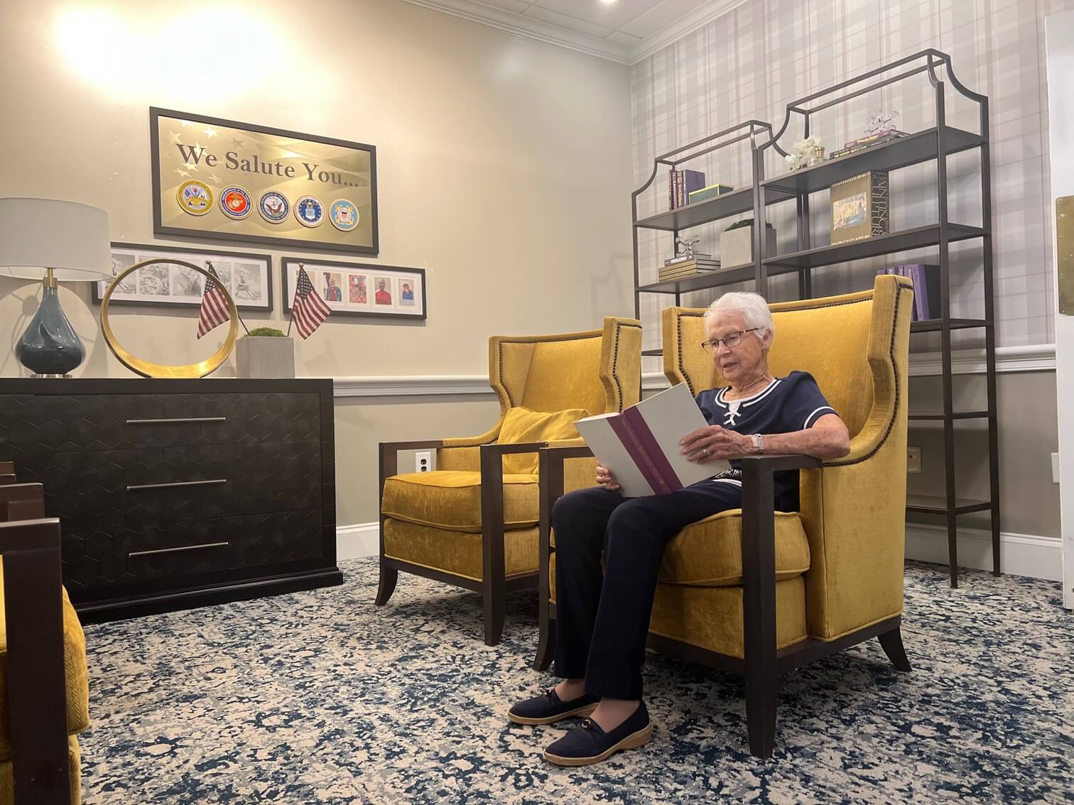 Senior woman reading and relaxing in a cozy living area with yellow chairs and bookshelves.