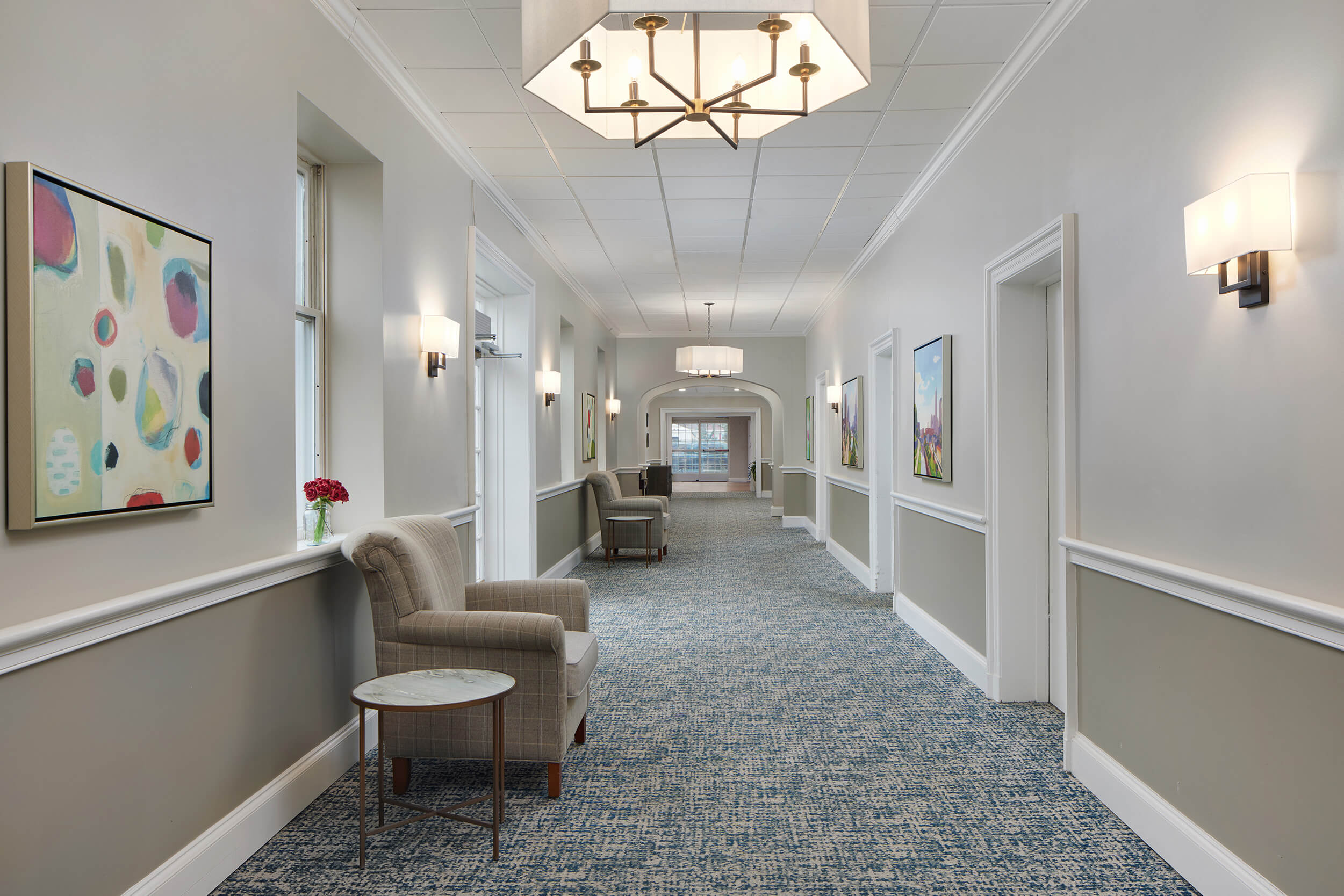 Elegant hallway with armchairs, modern artwork, and soft lighting in a senior living community.