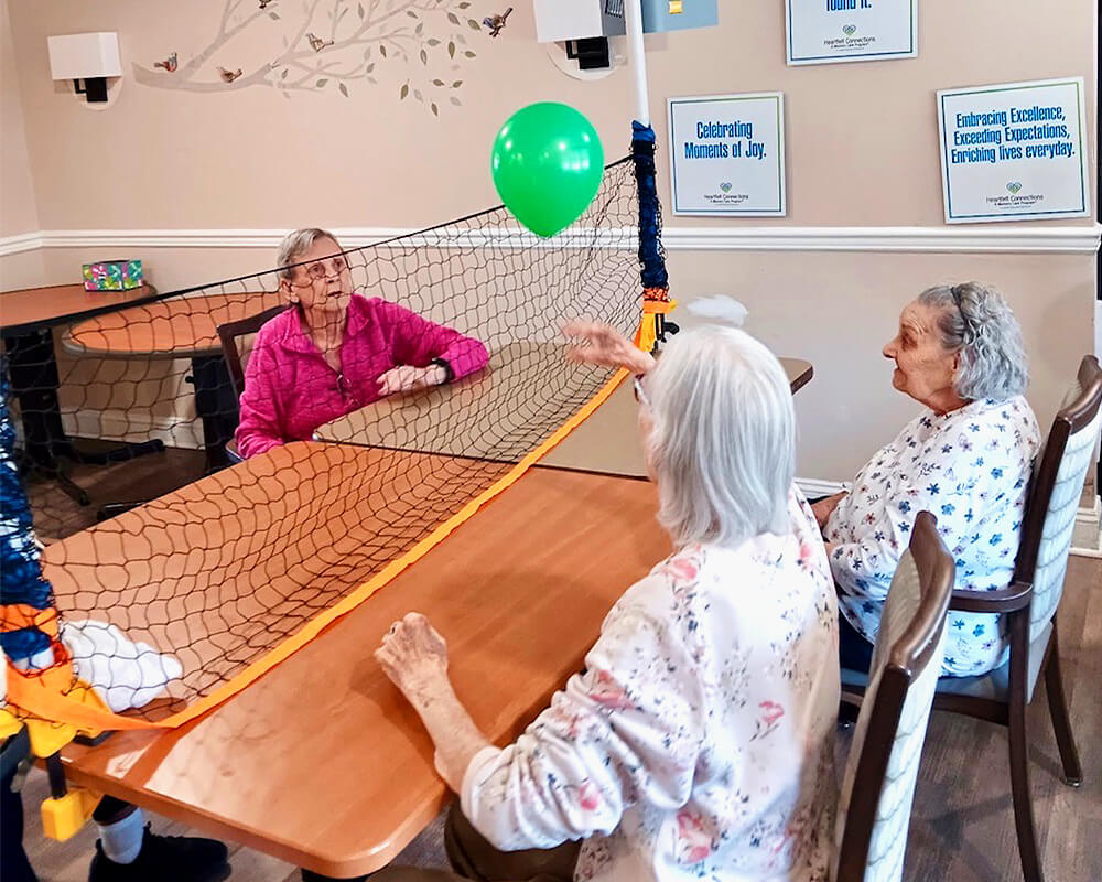 Seniors sit around a table and volley a balloon