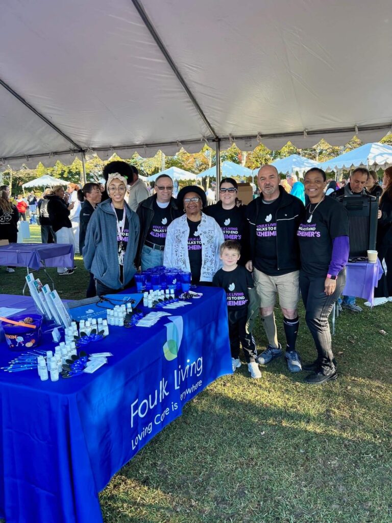 Group of people at a community event with a branded table under a tent.