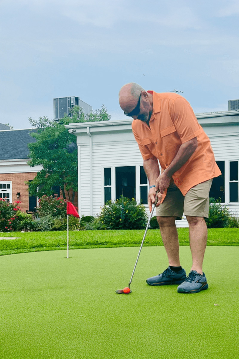 Man wearing orange shirt putting on a green at community courtyard.