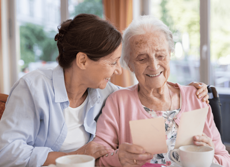 Elderly woman and younger woman sharing a joyful moment at a table in a senior community.